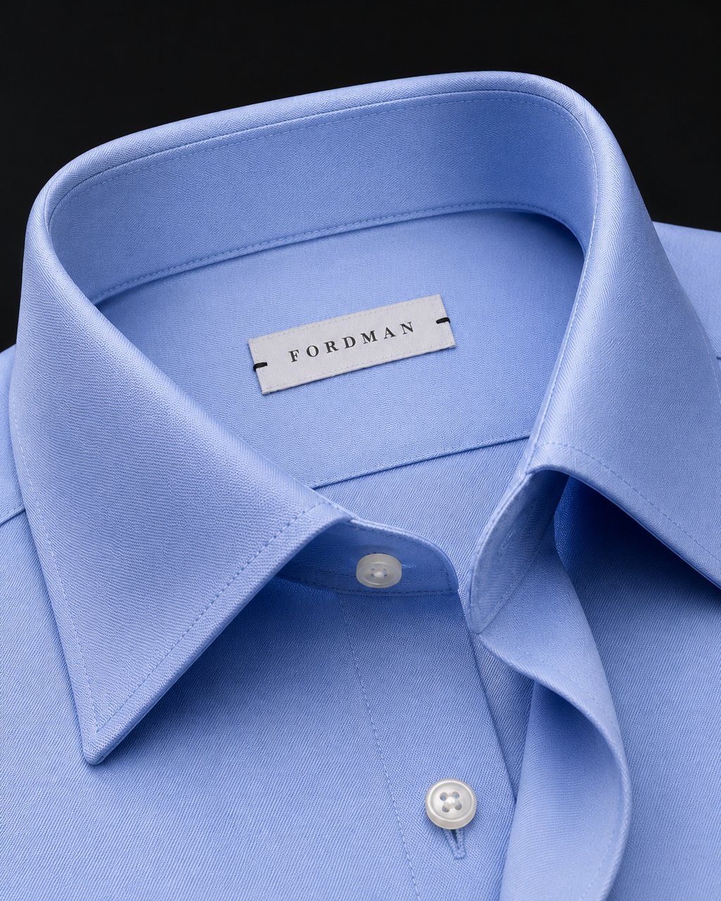 A close-up of a light blue dress shirt collar with a visible Fordman neck label, set against a dark background.